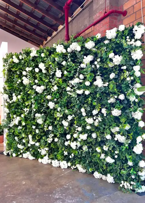A greenery wall of ivy and white roses installed as an event backdrop in a venue with exposed brick